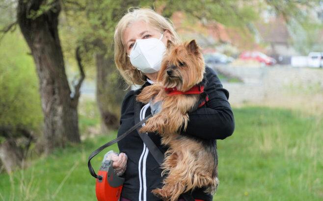 Woman wearing mask holding dog outside